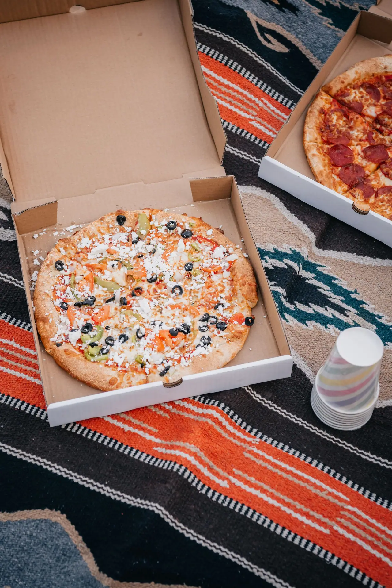Pizza in a kraft pizza box on a picnic rug